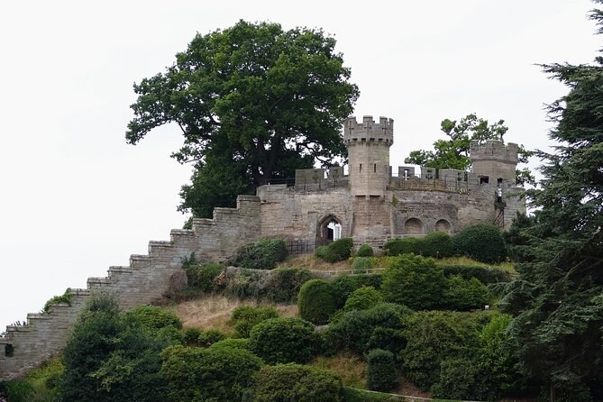 The curtain wall and a tower of Warwick Castle above the wooded mound